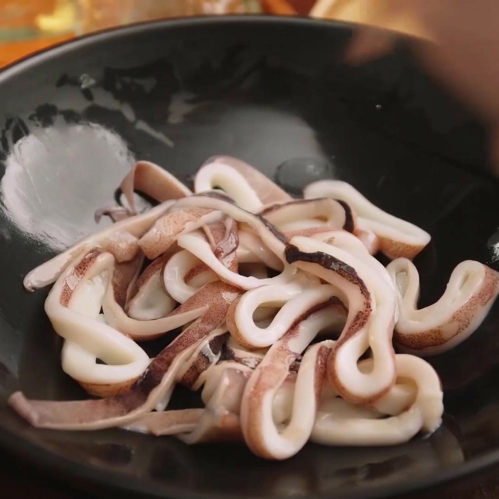 Slices of fresh squid rings sitting in a black bowl ready for seasoning.