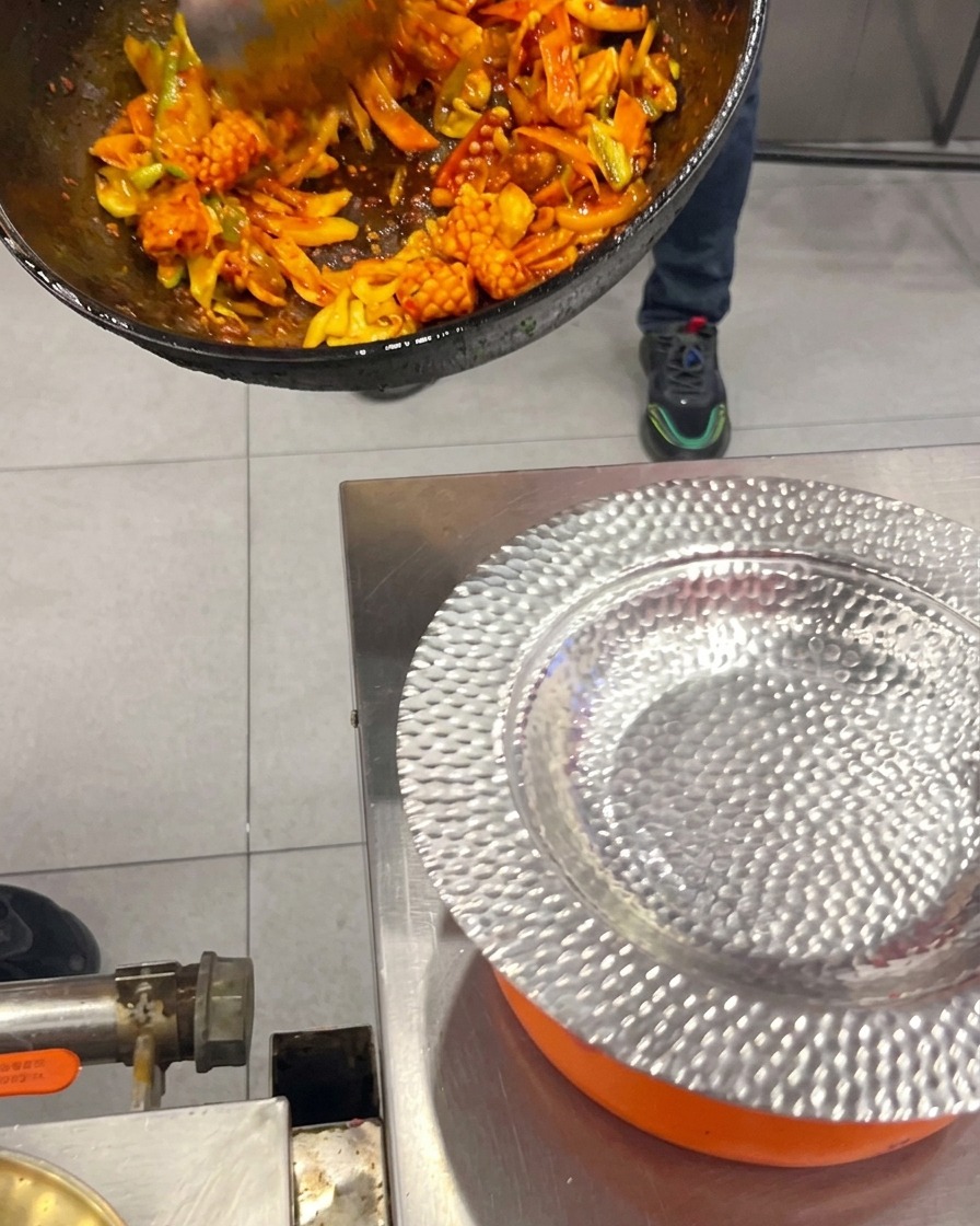 Stir-fried Korean spicy squid and pork belly with vegetables being scooped from a wok into a hammered silver plate.