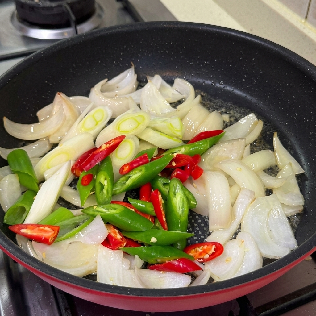 Sliced green and red chilies, scallions, and minced garlic cooking in a pan with the onions.