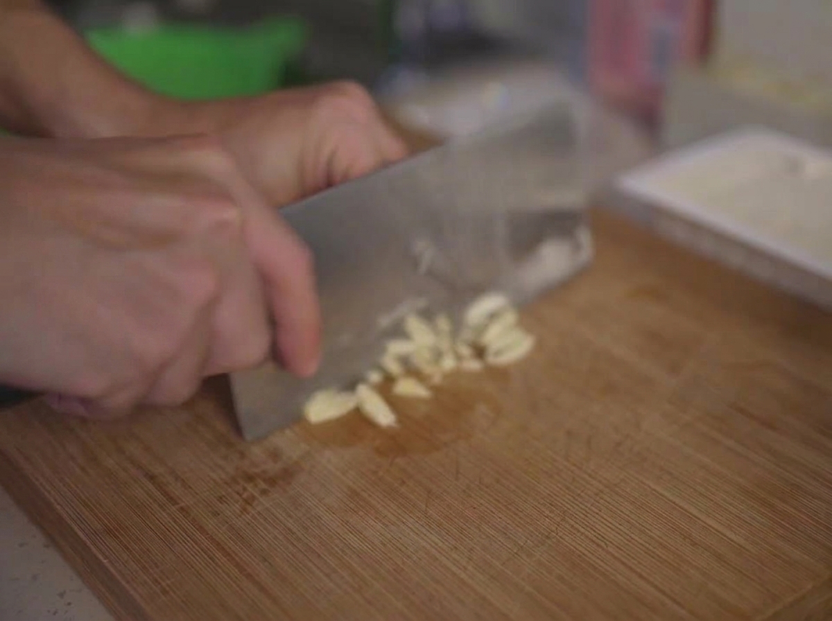Finely mincing garlic cloves on a wooden cutting board using a kitchen knife.