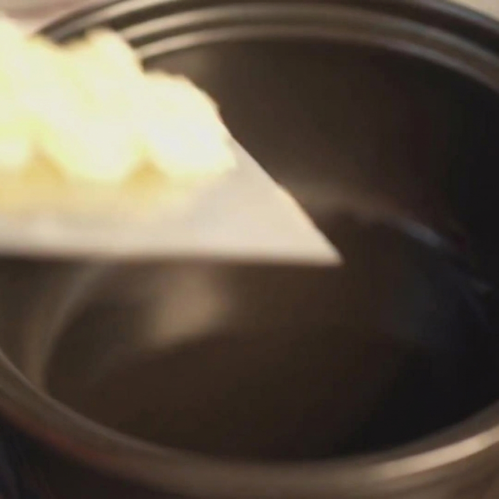 Finely minced garlic being added from a surface into a preheated black clay pot with shimmering oil.