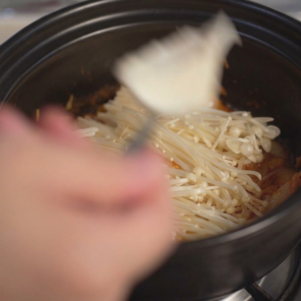 Scooping large chunks of soft white tofu into the pot using a spoon.