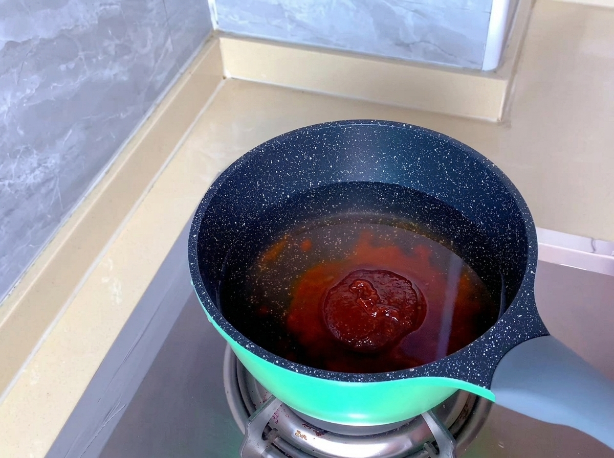 A clump of reddish-orange kimchi seasoning paste sits submerged in clear water within a speckled pot.