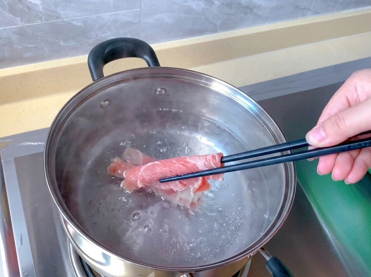 Chopsticks submerge a raw pink beef roll into a stainless steel pot of boiling water.