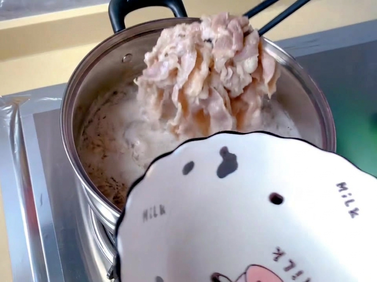Thinly sliced beef rolls being lifted out of a pot of boiling water covered with white foam using black chopsticks.