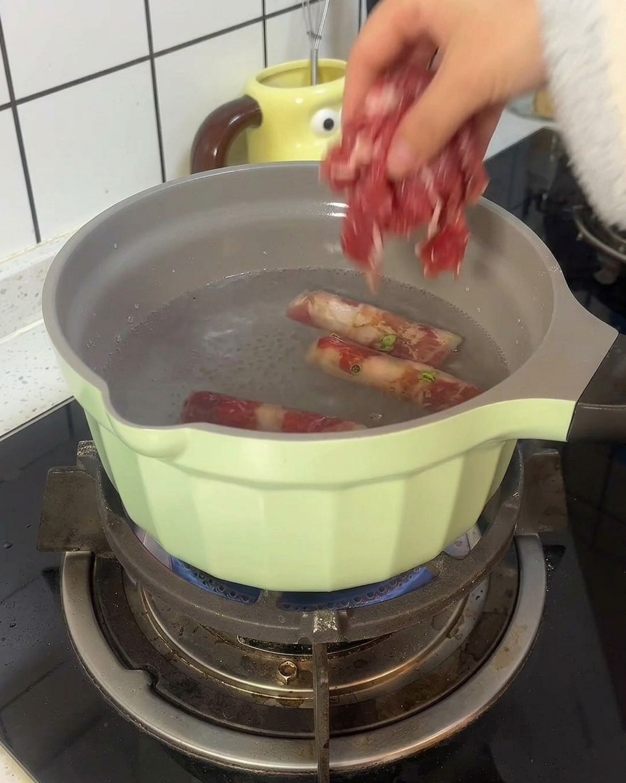 Beef rolls blanching in a light green pot of boiling water.