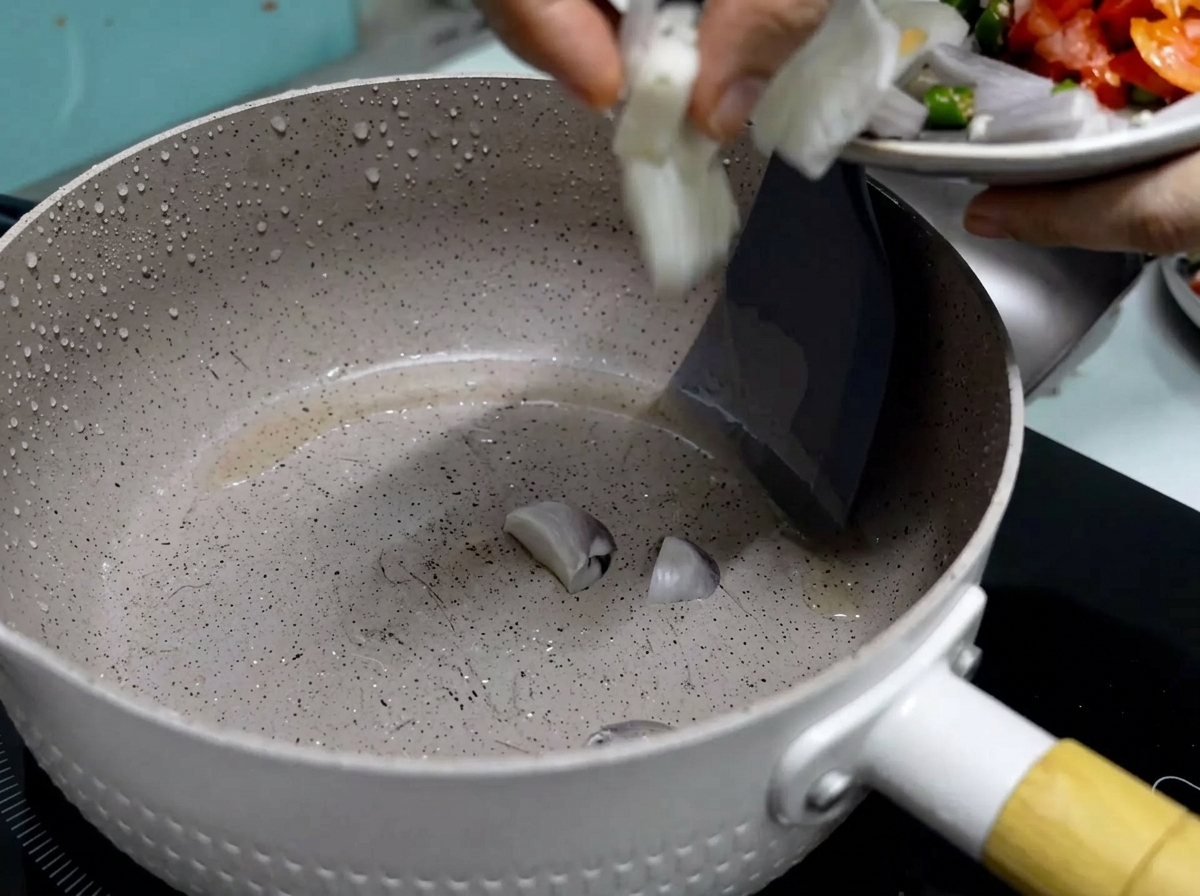 A hand sliding freshly cut red onions from a small plate into a heated non-stick pan with shimmering cooking oil.