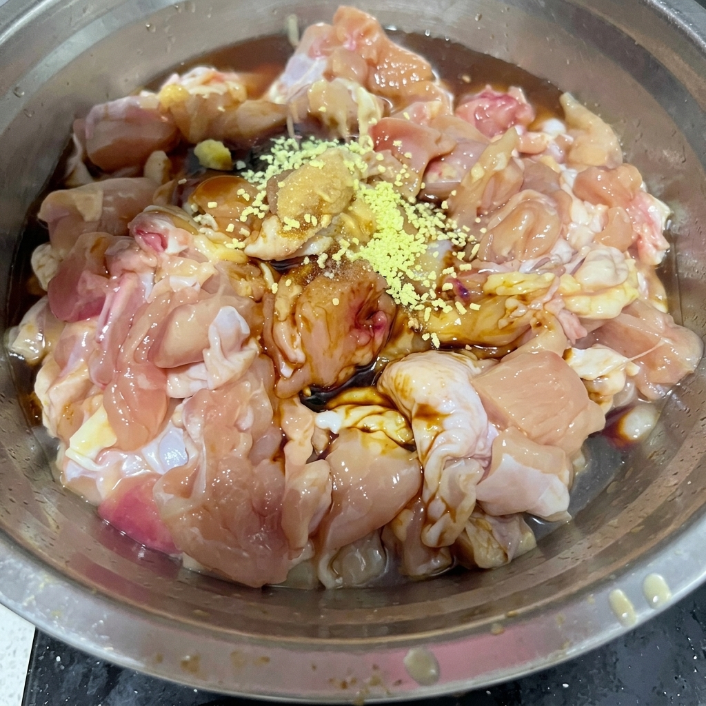 Yellow chicken bouillon powder and white salt sprinkled over the raw chicken pieces in a metal bowl.