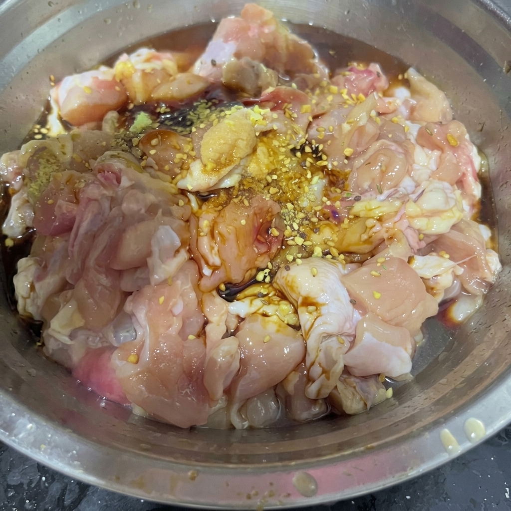 A spoonful of dry barbecue seasoning blend scattered over marinated chicken pieces inside a stainless steel mixing bowl.
