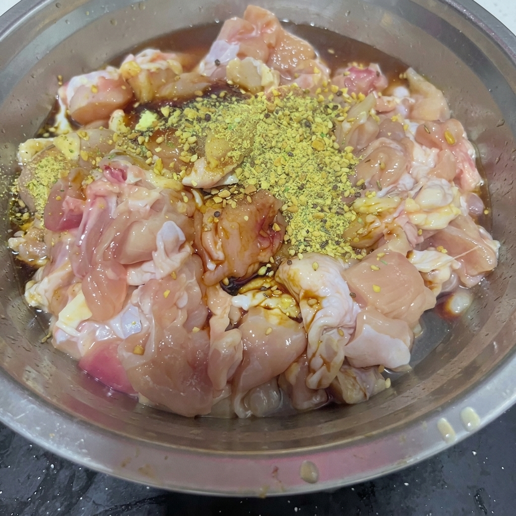 White granulated sugar sprinkled over the seasoned chicken thigh mixture in a stainless steel bowl.