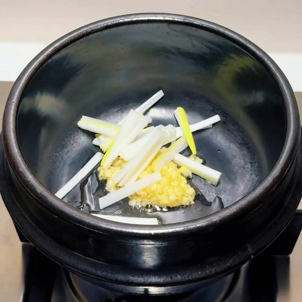 Thinly sliced white and pale green strips of garlic shoots layered over a mound of minced garlic in a black pot.
