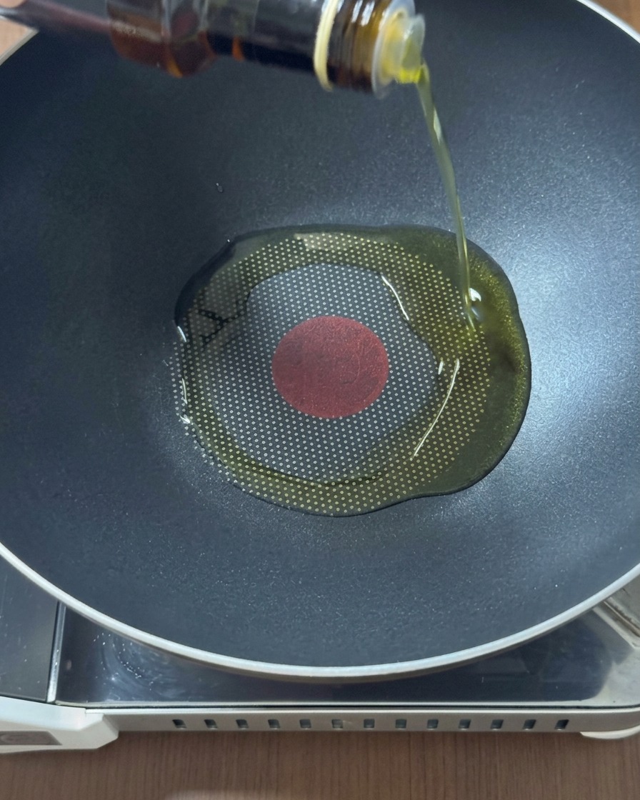 Pouring golden oil from a glass bottle into the center of a heated black wok.