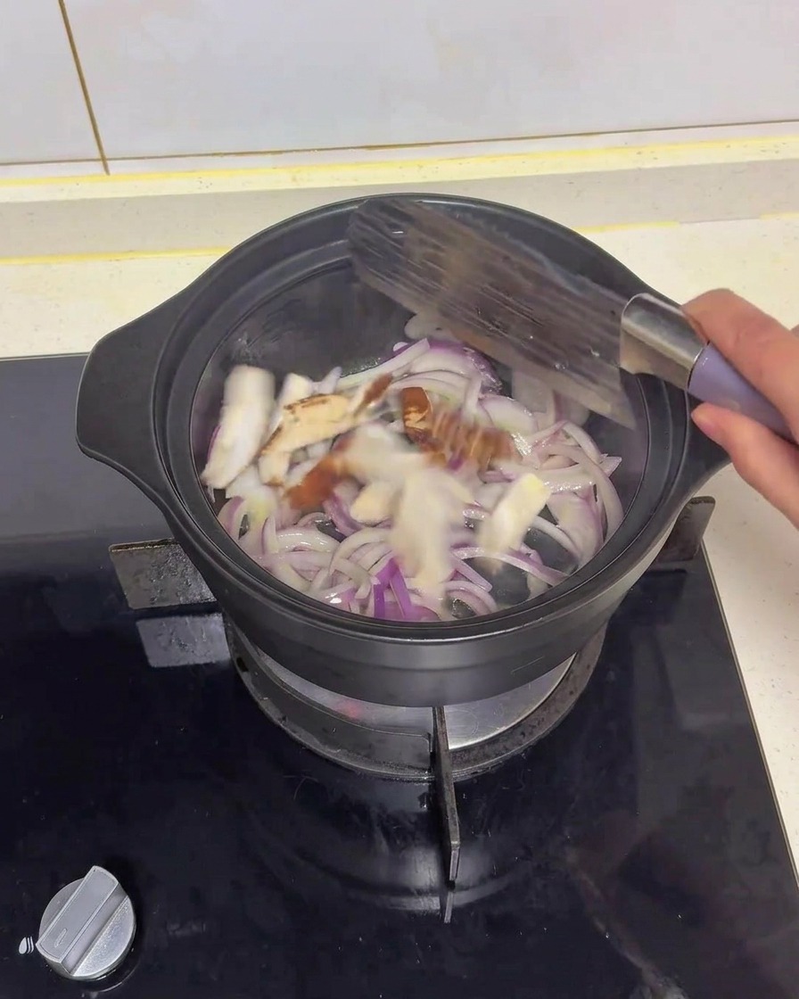 Sliced shiitake mushrooms being tossed and stir-fried with red onions in a black pot using a spatula.
