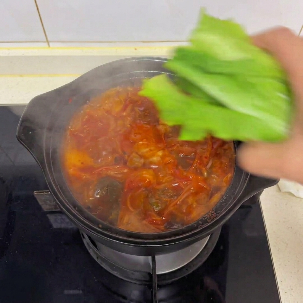 A hand dropping fresh green romaine lettuce leaves into a steaming hot pot of kimchi tofu soup.