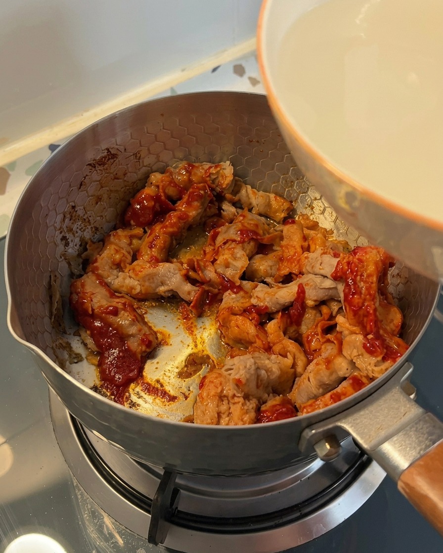Cloudy rice-washing water being poured from a white bowl into a pot filled with seasoned beef.