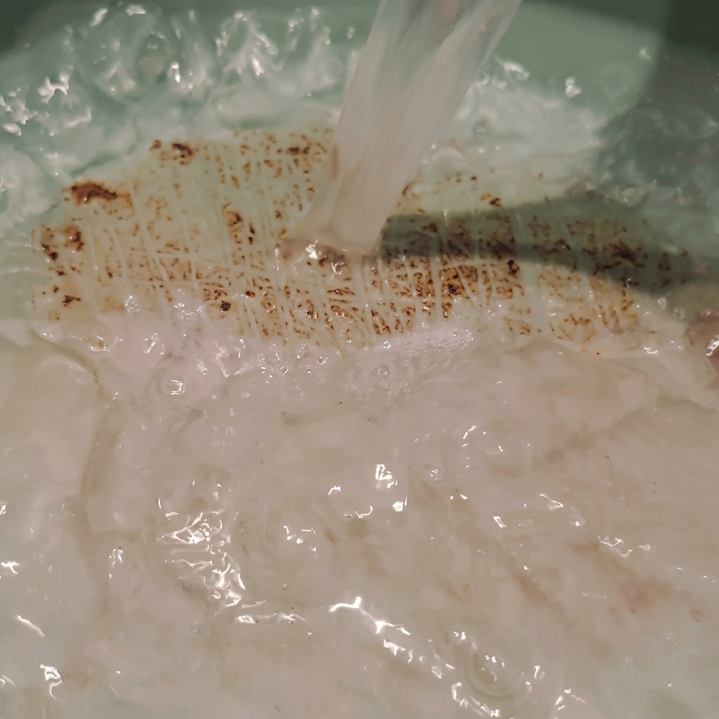 Cloudy rice water being poured directly into a cooking pot, creating soft ripples and bubbles in the liquid.