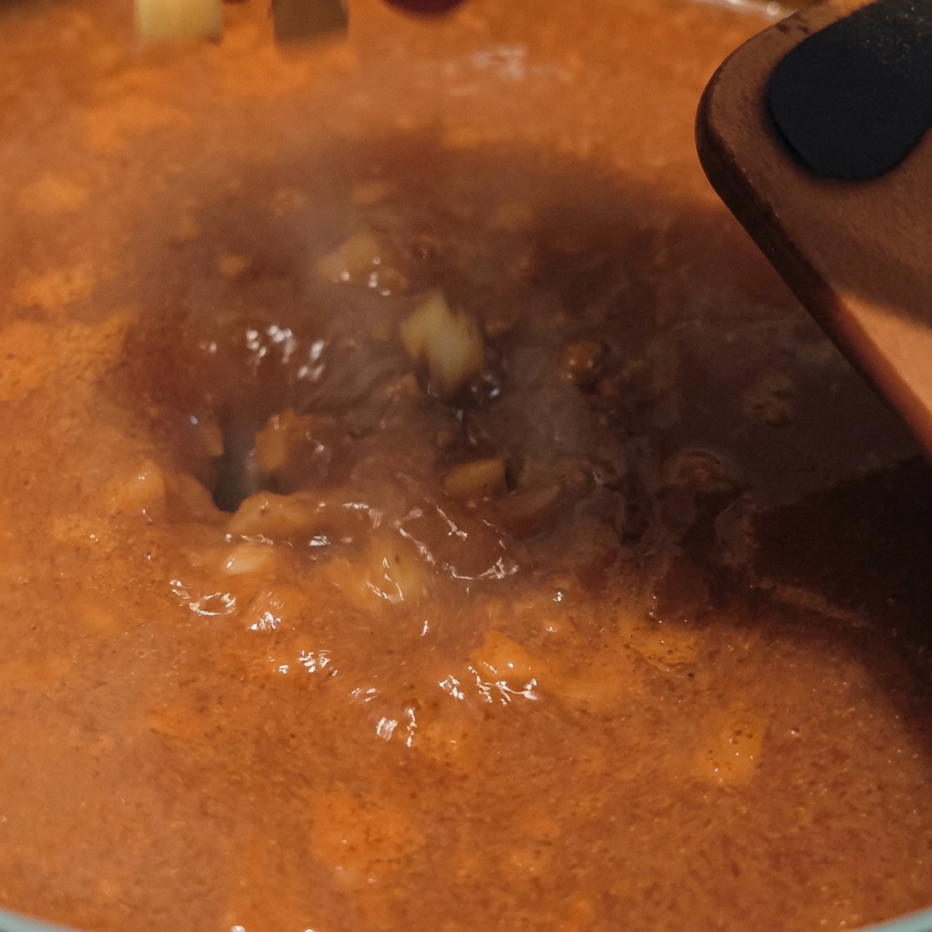 Diced raw potatoes being dropped into a bubbling, orange-colored savory soup base with steam rising from the pot.