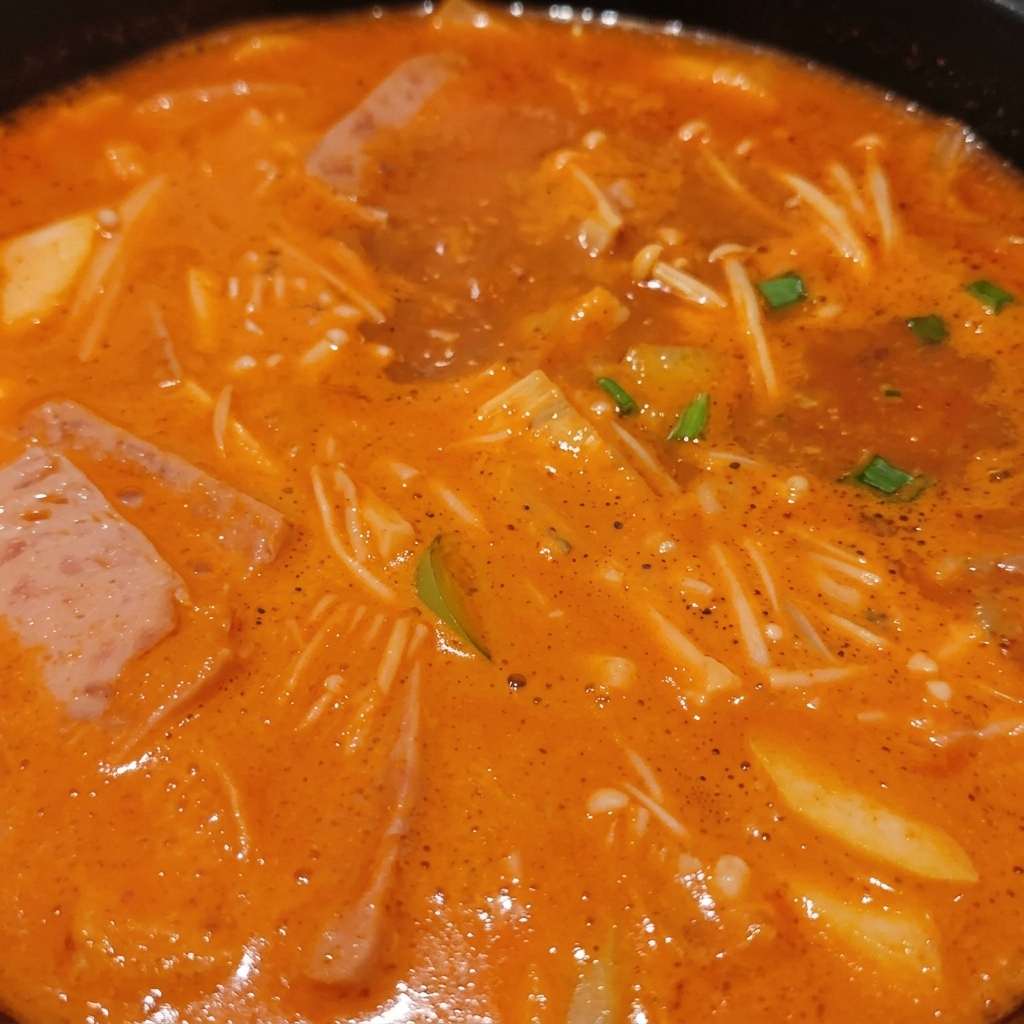 A bubbling Korean stew packed with enoki mushrooms, slices of meat, green scallions, and tofu submerged in a rich orange broth.