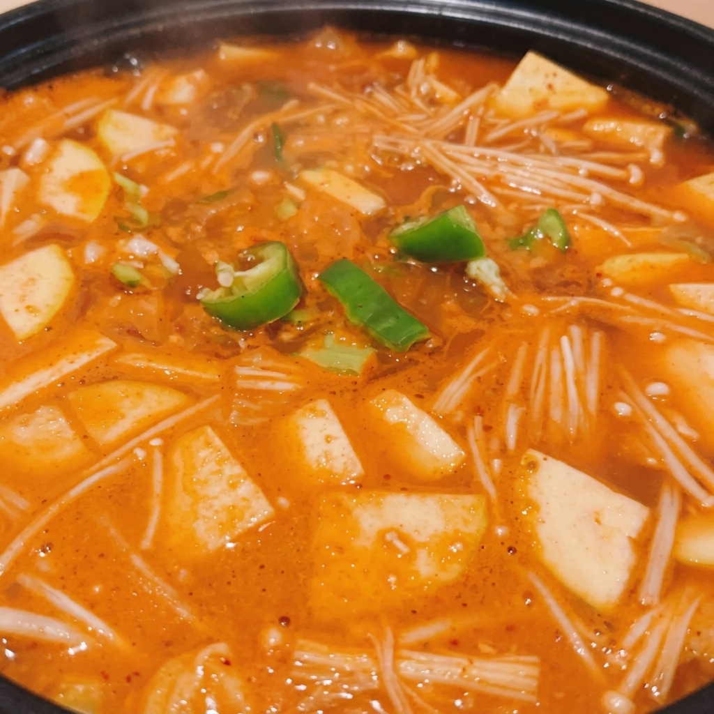 A black pot of simmering Korean soybean paste stew topped with fresh green chili rings.