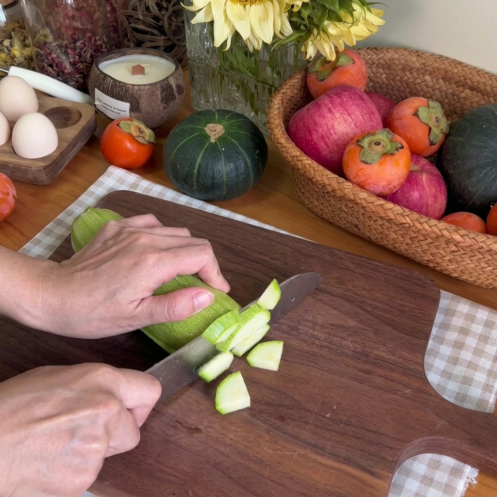 A close-up view of hands using a chefs knife to chop a green zucchini into small pieces on a wooden cutting board.