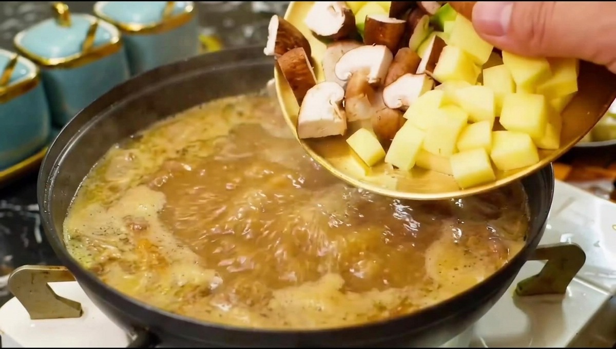 Chopped mushrooms and vegetables being slid from a plate into a boiling pot of seasoned broth.