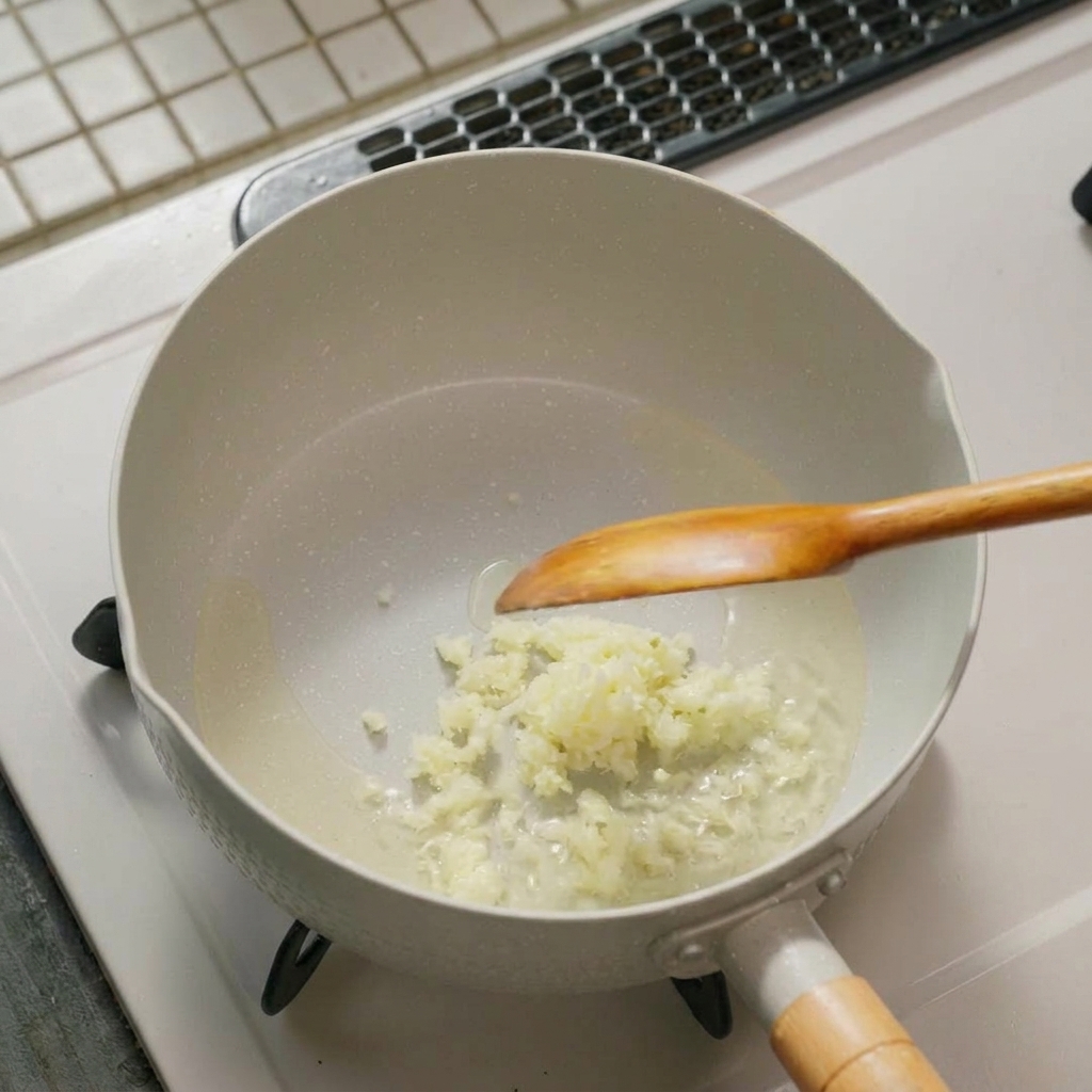 Finely minced garlic and green onions sizzling in oil at the bottom of a white pan with a wooden spoon resting inside.