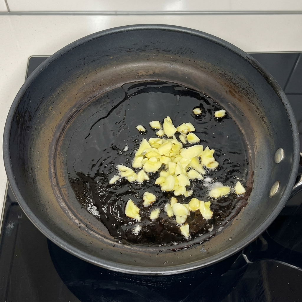 Finely minced garlic pieces sizzling in a pool of hot cooking oil inside a dark frying pan.