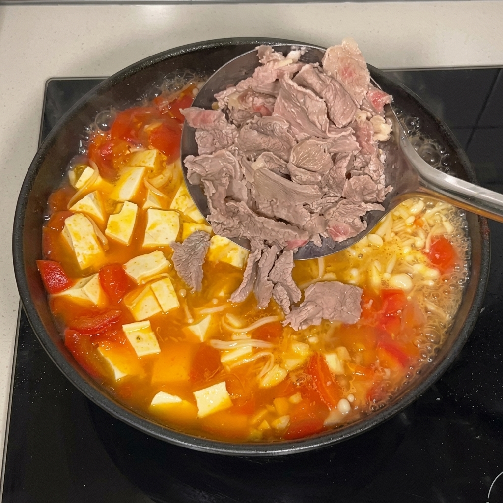A metal slotted ladle placing thinly sliced blanched beef into a bubbling pan of tomato broth filled with enoki mushrooms and cubed tofu.