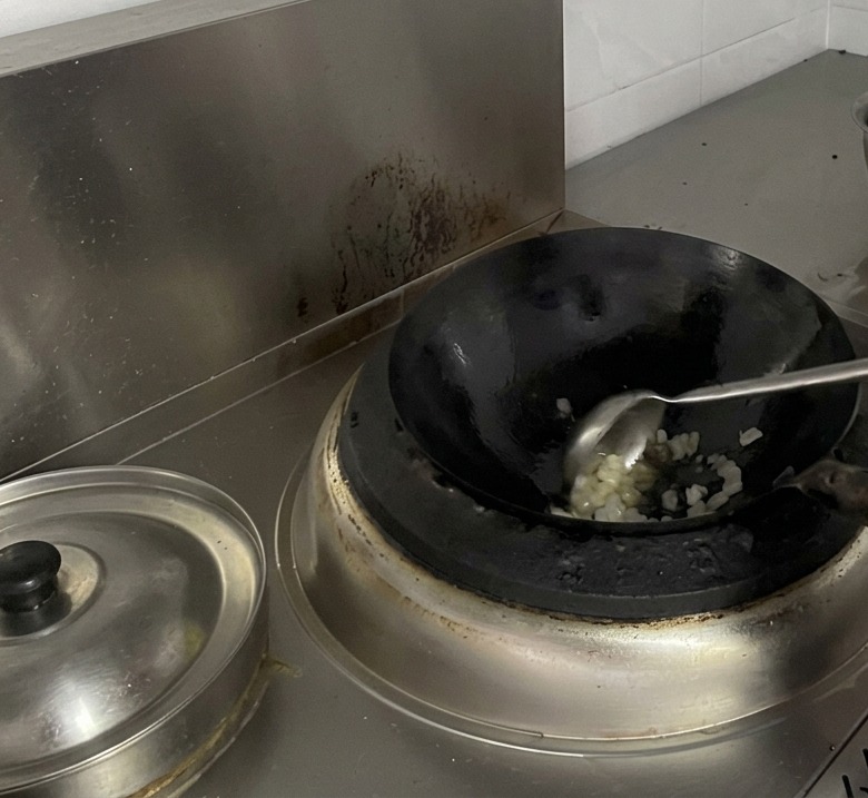 A cook using a large metal ladle to stir melting pieces of rock sugar in a wok.