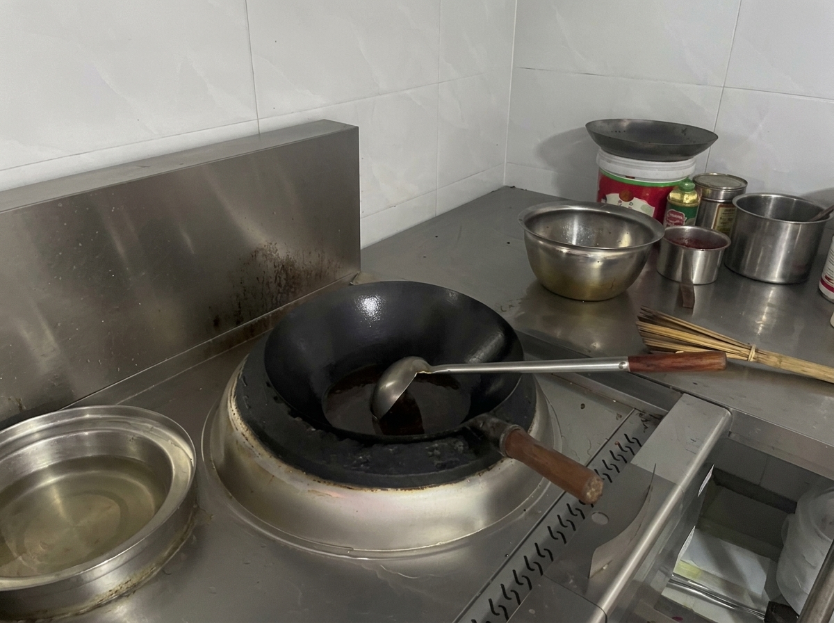 A black wok on a stove filled with a dark red-brown simmering liquid.