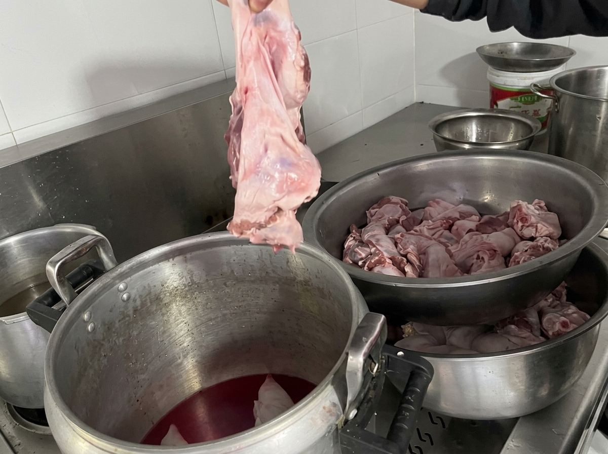 A hand holding up a large piece of raw diaphragm meat, ready to lower it into a stockpot containing pig trotters and broth.