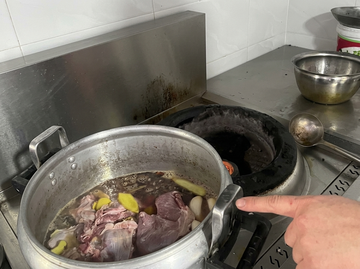 A large aluminum stockpot filled with raw meats, ginger slices, and dark broth sitting on a stove.