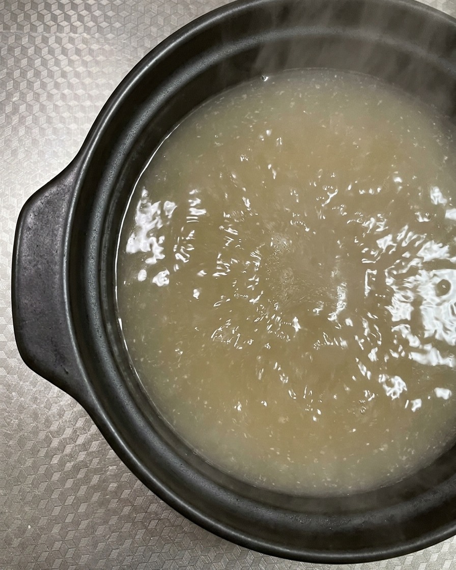 Thin slices of raw, marbled pork belly being placed into a bubbling clay pot of broth.