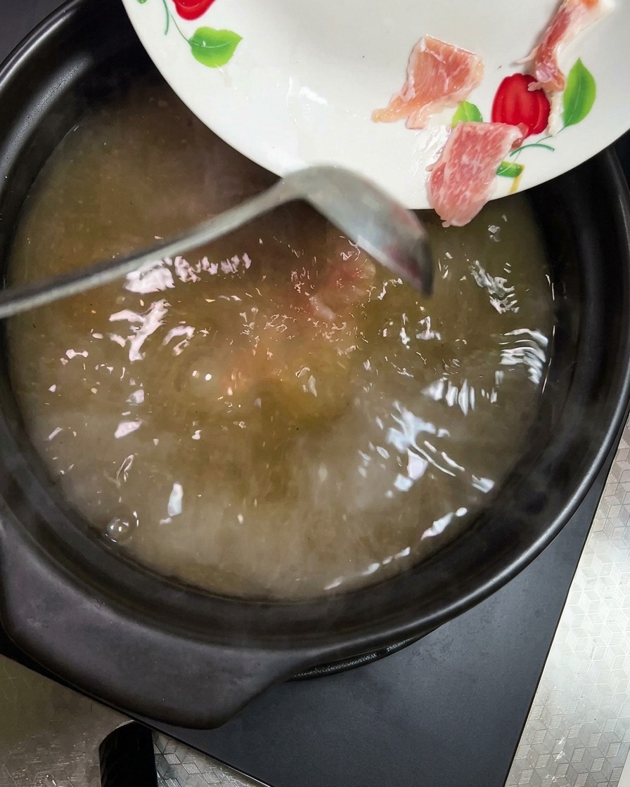 Chunks of bright orange carrot and pale yellow potato being added to the simmering soup.