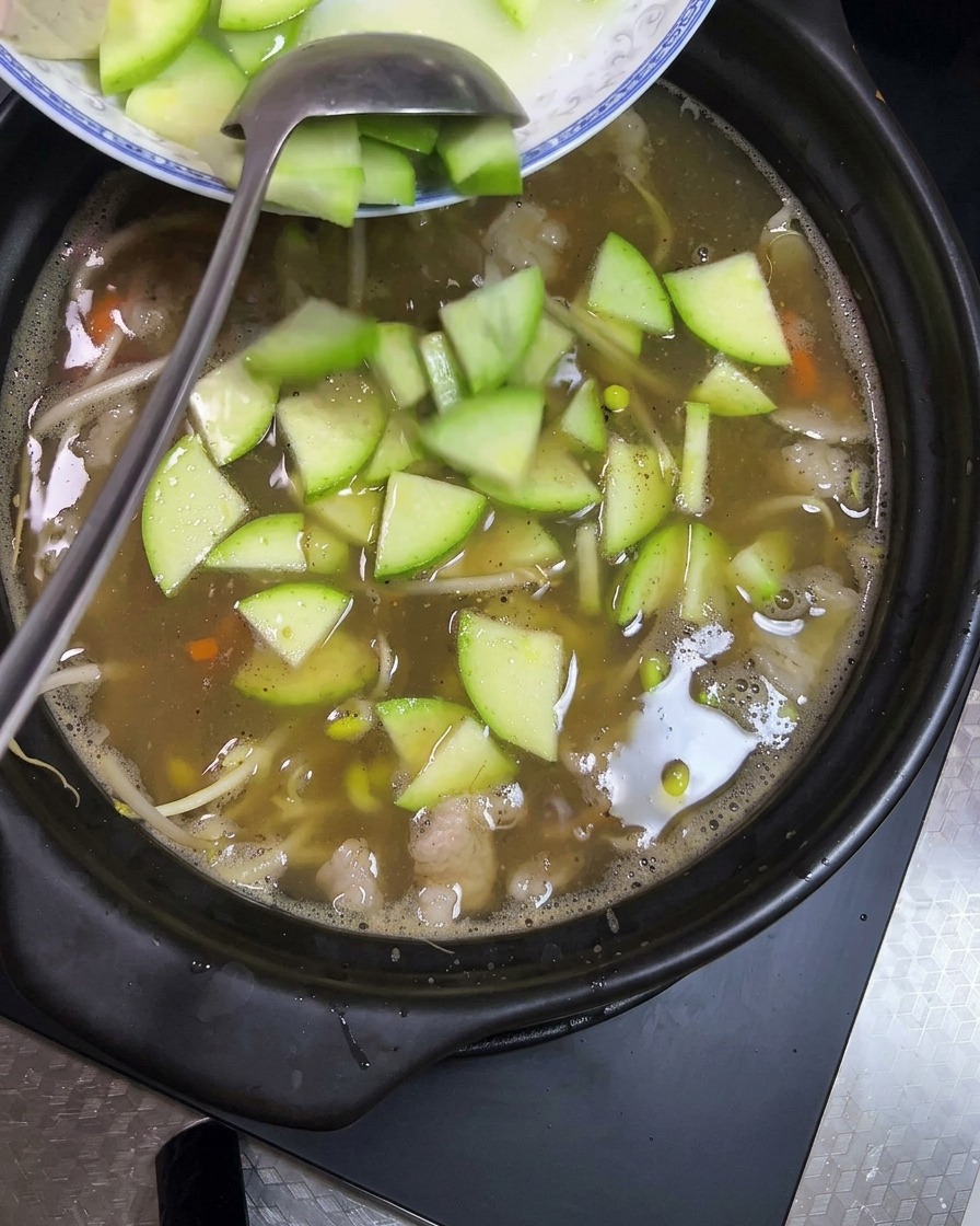 Cubed tofu and sliced green zucchini being added to the clay pot containing the bubbling stew.