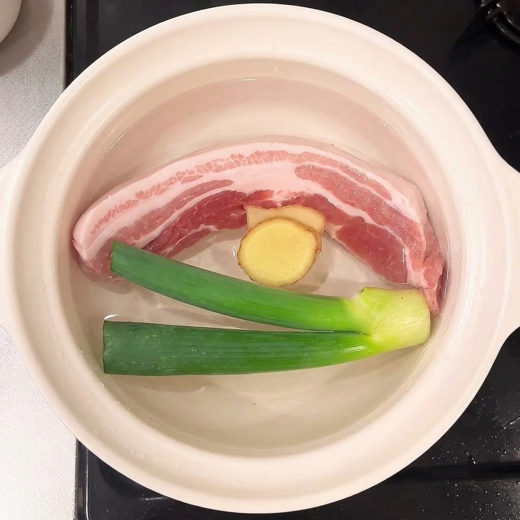 Scallions and ginger slices floating in the water alongside the pork belly.