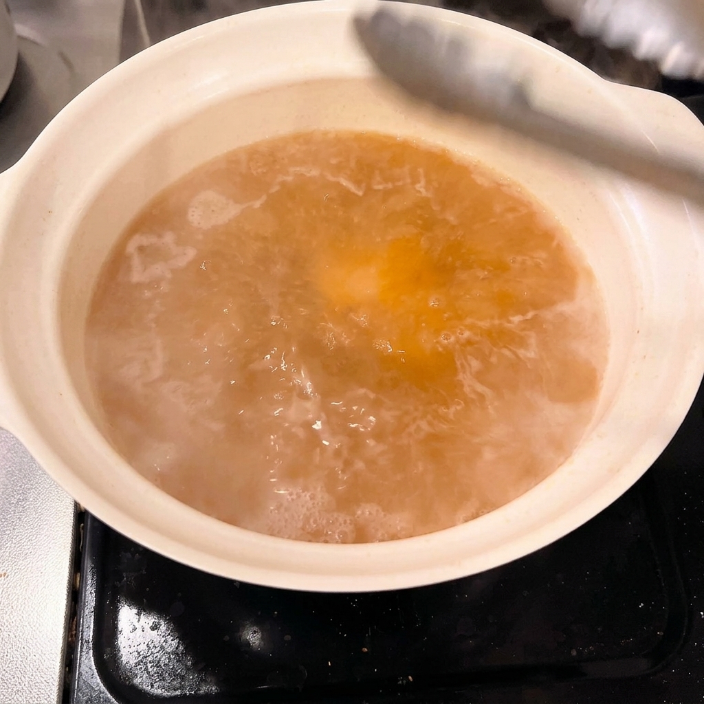Thick chunks of blanched pork belly being carefully placed into a pot of seasoned miso broth with tongs.
