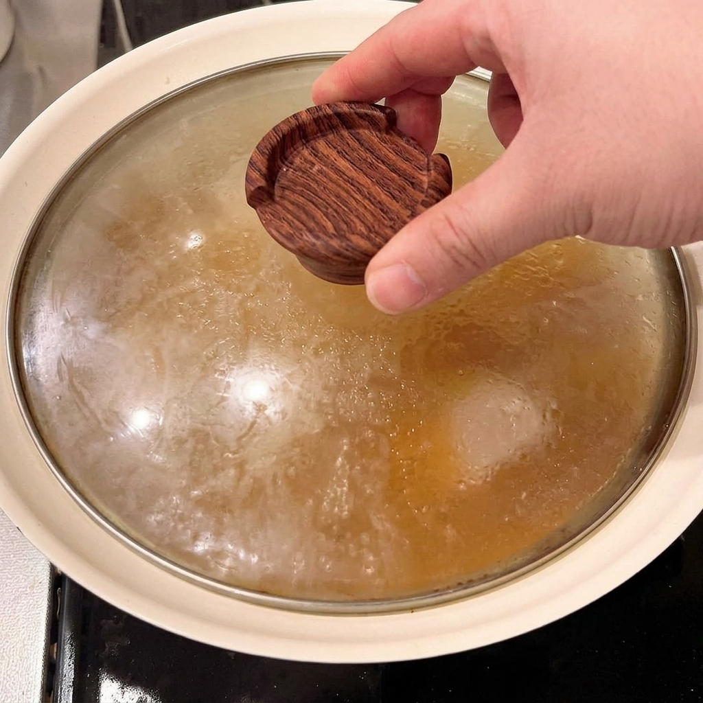 A small wooden drop lid being placed directly over the pork belly chunks simmering in the seasoned broth.