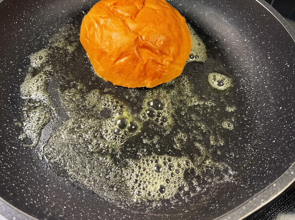 A burger bun toasting in a hot pan with melted butter, turning golden brown.