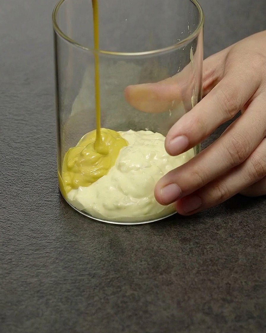 A pale yellow creamy burger sauce being stirred inside a clear glass mixing glass.