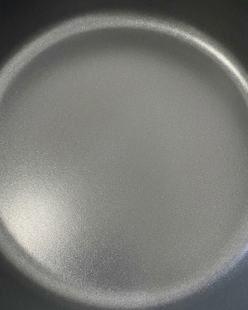Two slices of cheddar cheese melting beautifully over seasoned beef patties in a dark skillet.