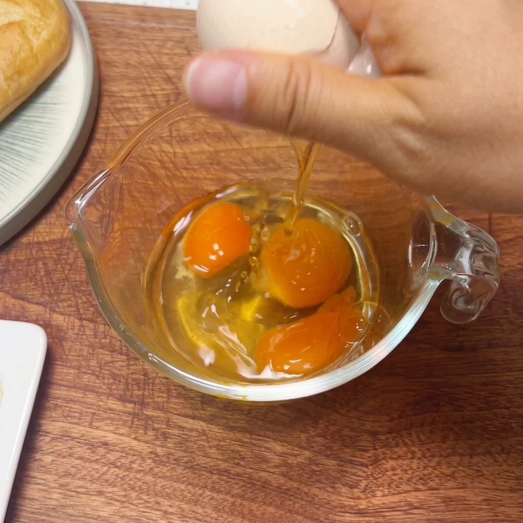 Three raw eggs in a glass measuring cup being whisked with chopsticks.