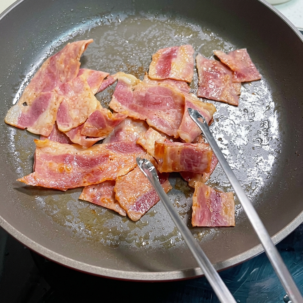 Whisked eggs cooking in a pan with bacon pieces.