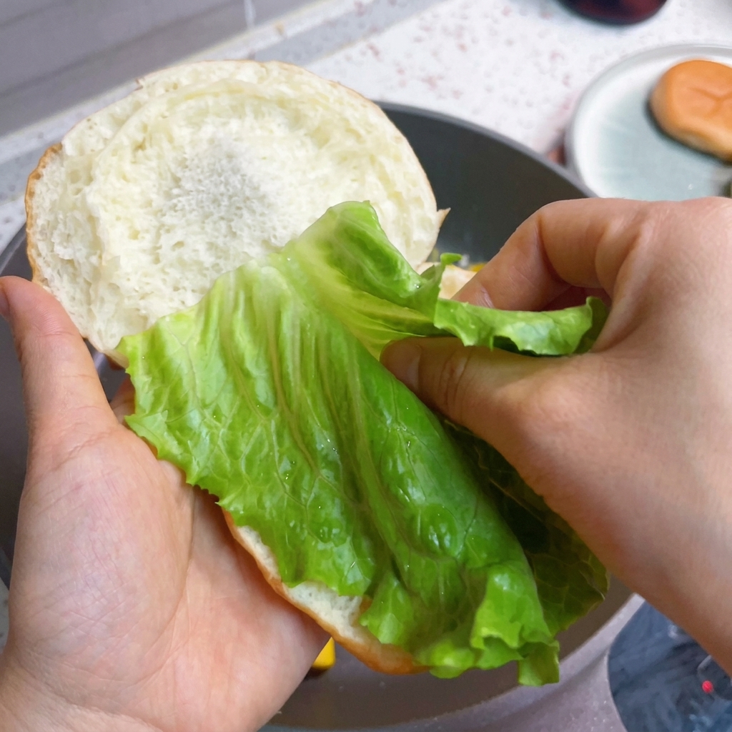 Assembling the burger with fresh lettuce, bacon, and fluffy eggs on a bun.