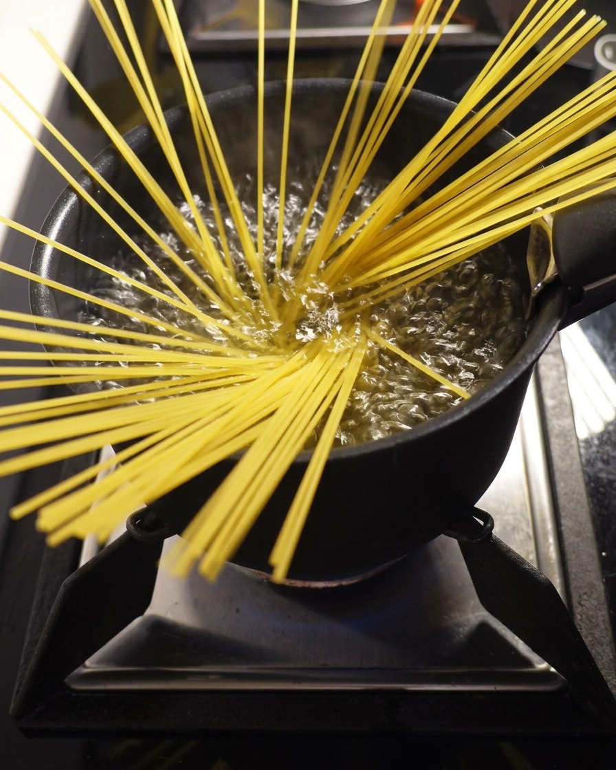 Dry spaghetti pasta being submerged into a large pot of boiling water.