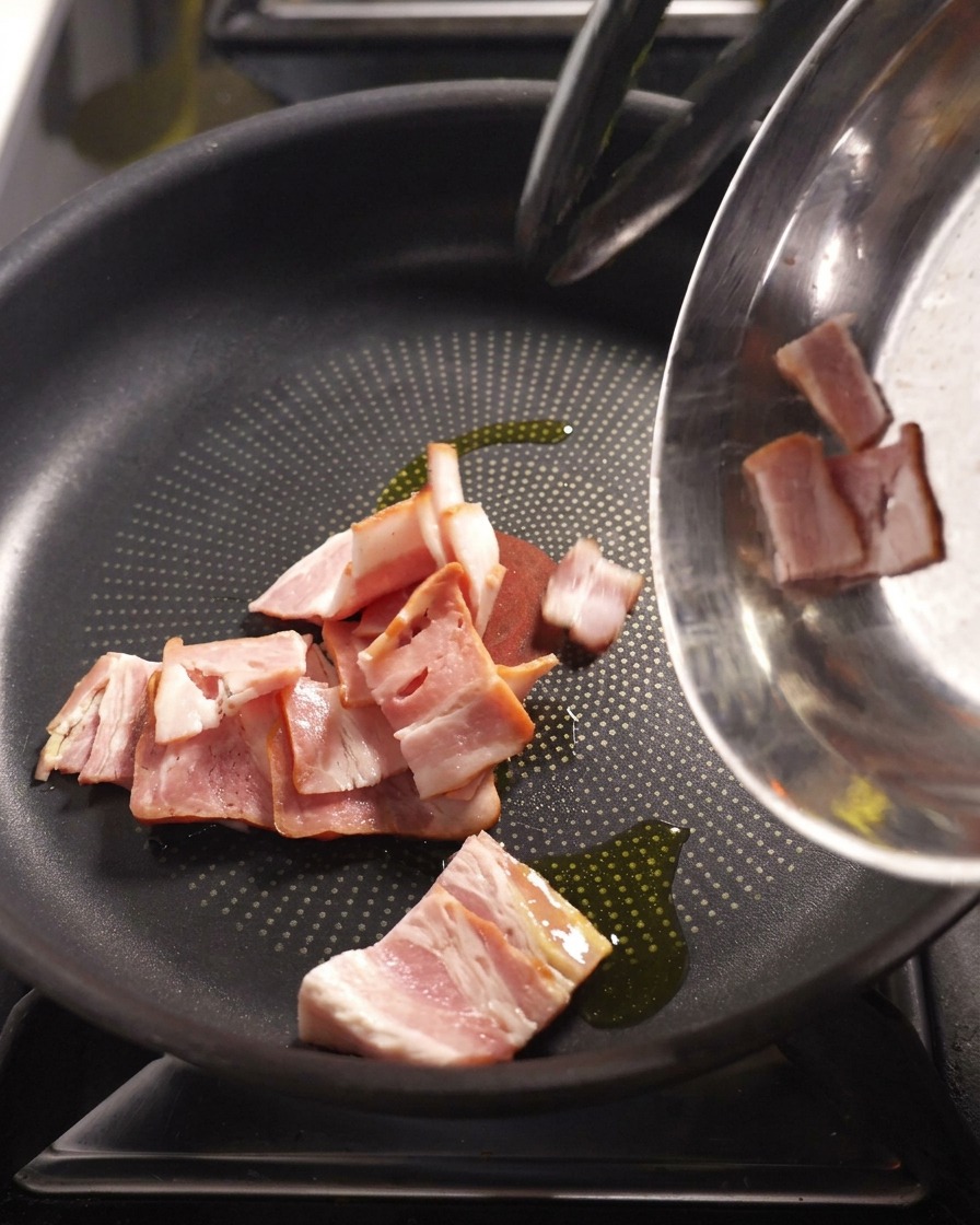 Bacon strips frying in a pan until browned and crispy.