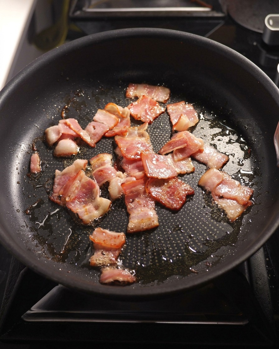Diced onions and minced garlic being sautéed in a pan with fried bacon.