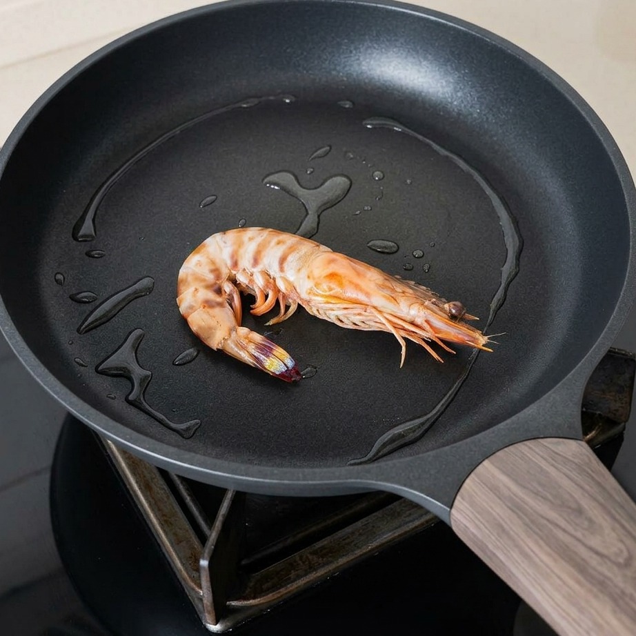 Two large prawns sizzling in a hot skillet with oil, seasoned with black pepper and herbs.