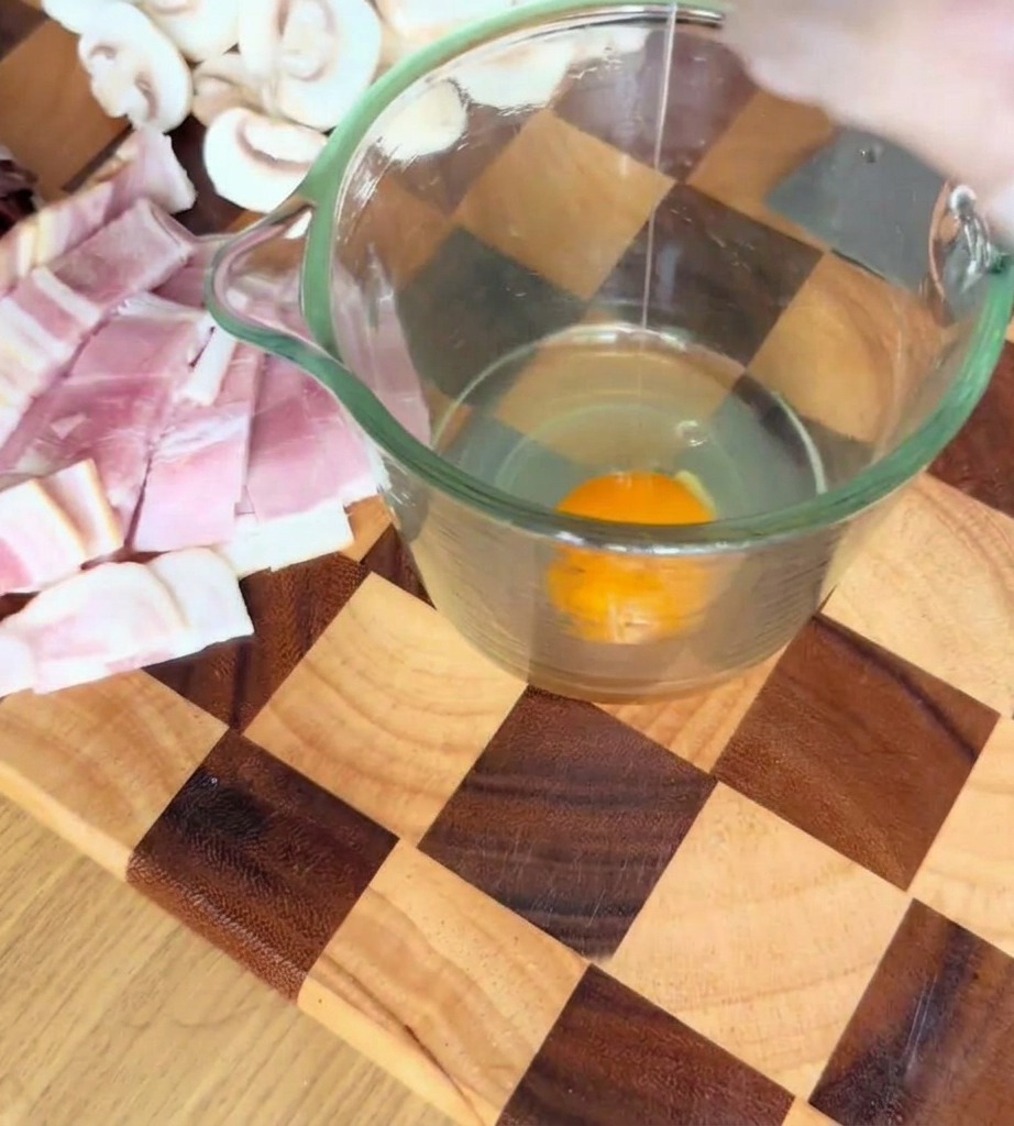 Eggs, parmesan cheese, and black truffle sauce being whisked together in a glass measuring cup.