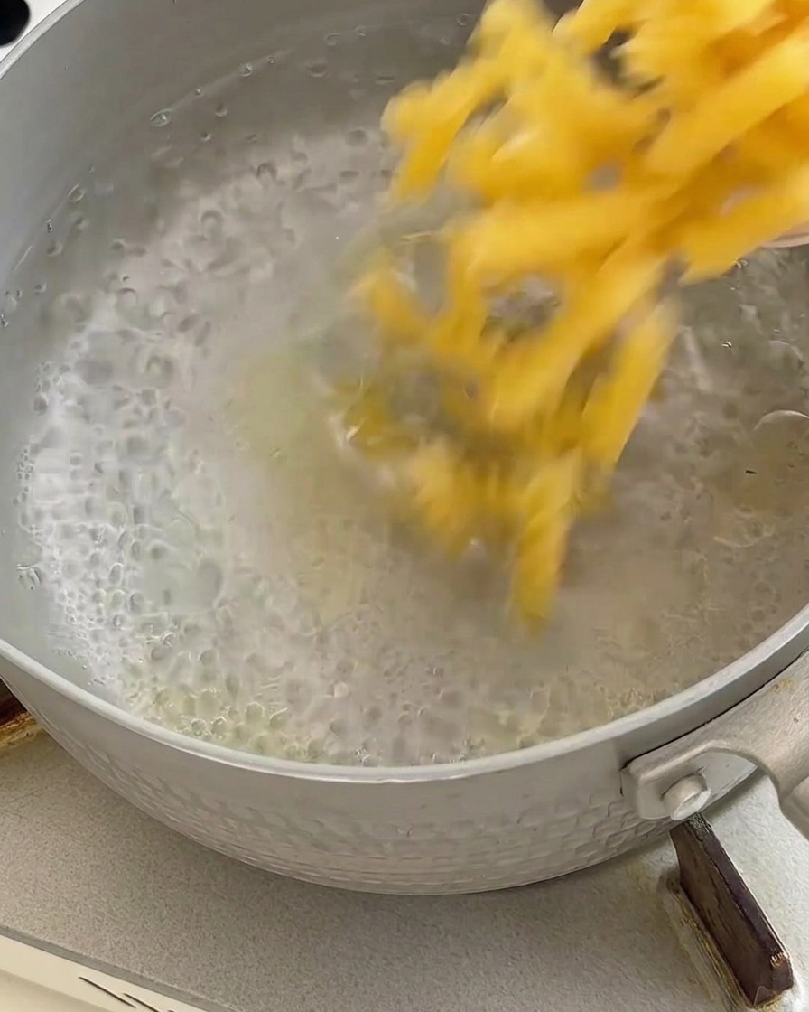 Cooked pasta being drained in a metal strainer after boiling in water.